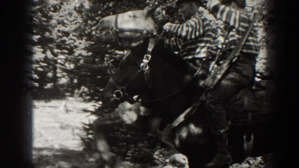 1938 California 8mm frame showing a man beside a saddled horse with a rifle in a forested mountain setting.