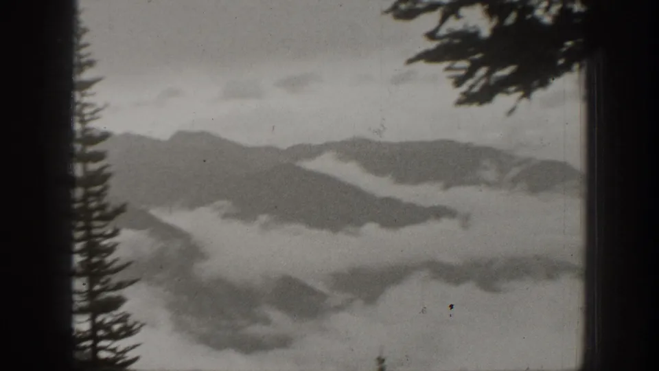 1938 California 8mm frame showing layered mountain ridges and low clouds viewed through dark vertical framing with pine silhouettes.