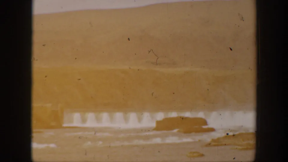 Warm-tinted 1938 California frame showing water pouring over a dam or spillway, with dark framing and aged film marks.