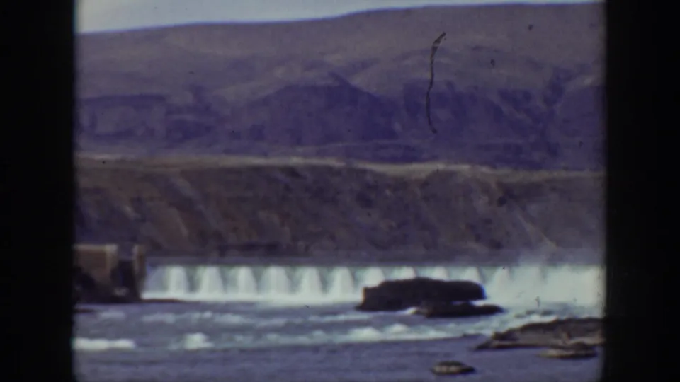 1938 California home-movie view of a dam spillway, white water, dark rocks, and a dry-looking hillside backdrop.