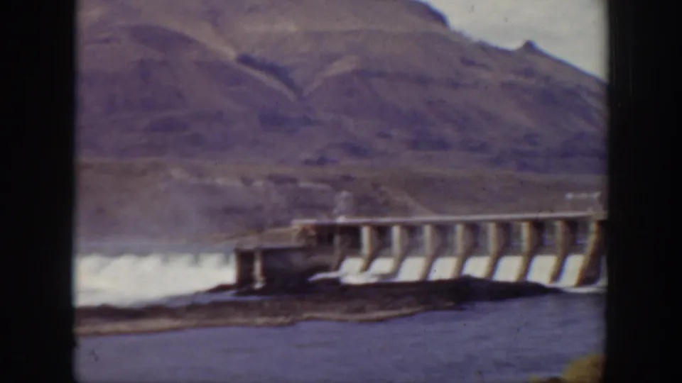 1938 California 8mm frame showing dam spillway water rushing across a rocky mountain landscape.