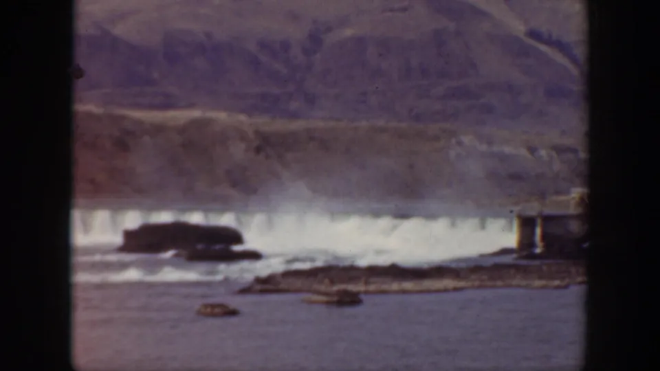 Vintage 8mm view of a California waterfall spilling across a rocky channel with a hillside in the background.