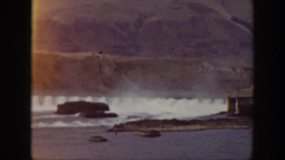 Faded 1938 California home-movie frame with waterfall spray, rocky water, and distant hillside under soft exposure.