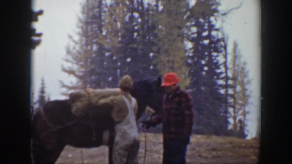 The man in white overalls and the man in a red hat remain beside a dark horse on a California forest slope in this 1938 home movie frame.