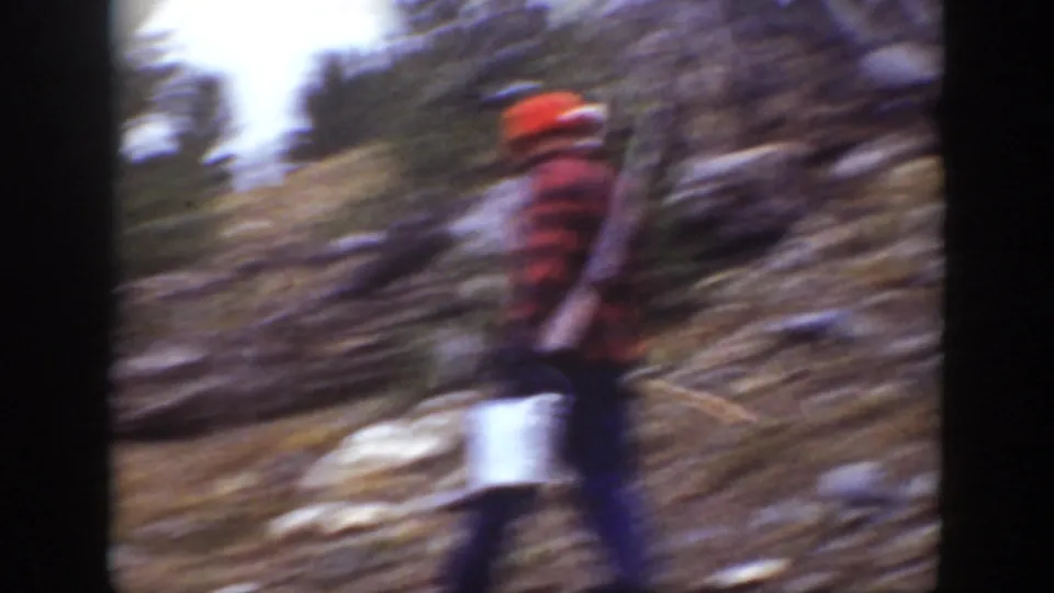 A man in a red hat and plaid shirt appears blurred while walking through rugged California mountain terrain.