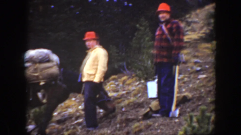Two men in red hats stand near a packed animal on a forested California mountain trail in 1938 home-movie footage.