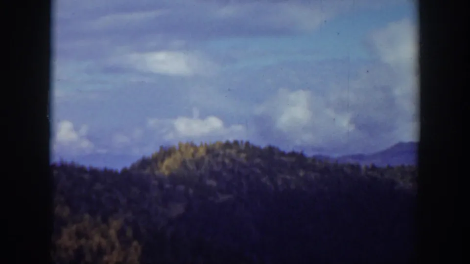 1938 California home-movie landscape frame showing wooded hills and distant ridges beneath a cloudy sky.