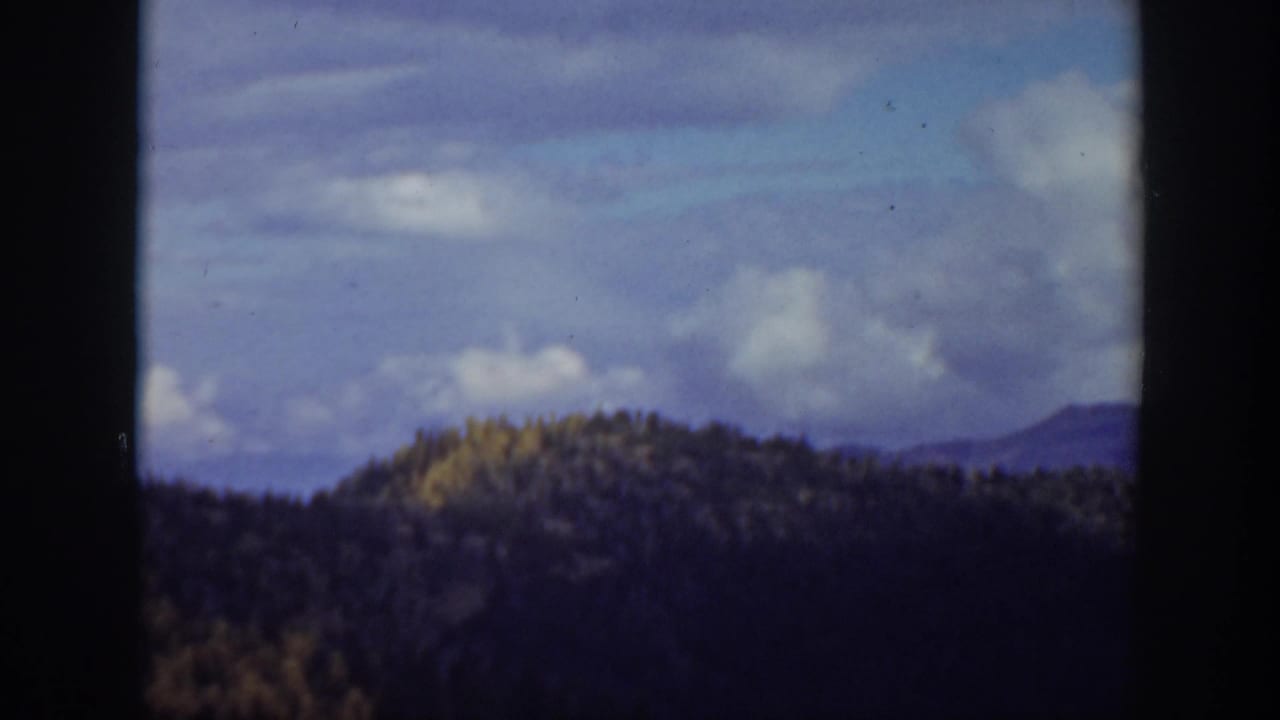 1938 California 8mm frame showing a forested ridge, distant hills, clouds, and visible film gate edges.