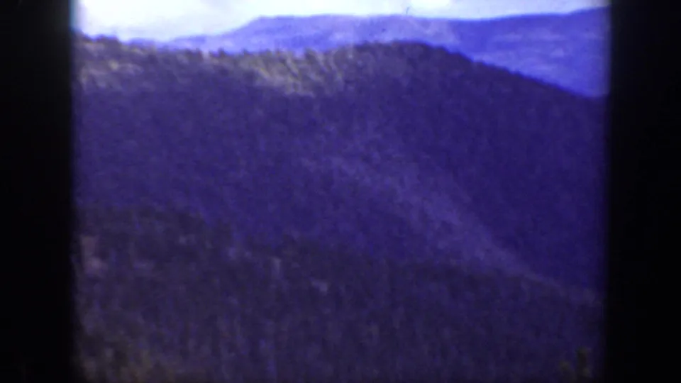 1938 California 8mm frame with a blue-purple forested hillside and layered mountain ridges in the distance.