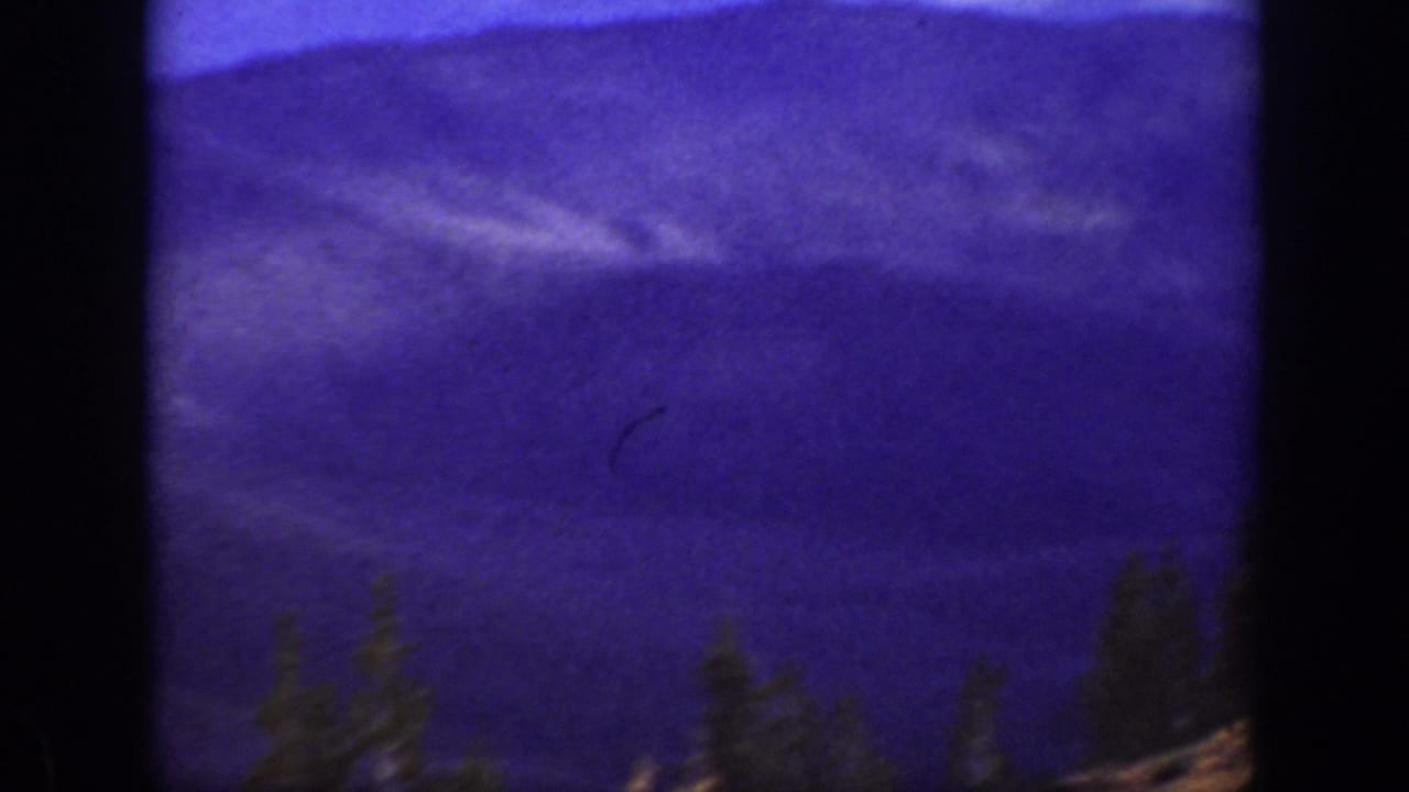 1938 California home-movie frame showing purple-toned mountain ridges and dark evergreens in soft focus.