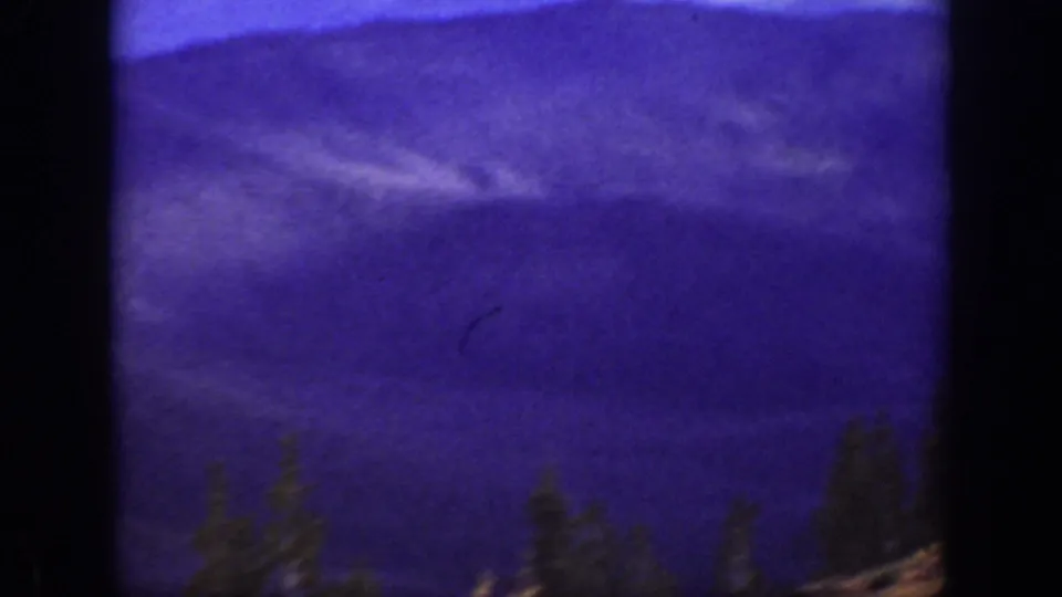 1938 California home-movie frame showing purple-toned mountain ridges and dark evergreens in soft focus.