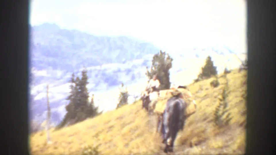 1938 California home-movie frame with a distant person riding a loaded mule or horse on a mountain trail.