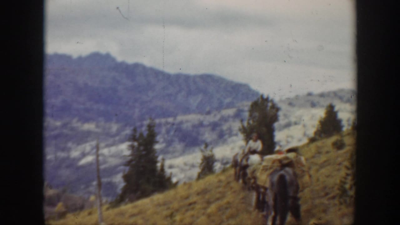 1938 California 8mm frame showing a man riding with a pack animal on a sloped mountain trail under an overcast sky.