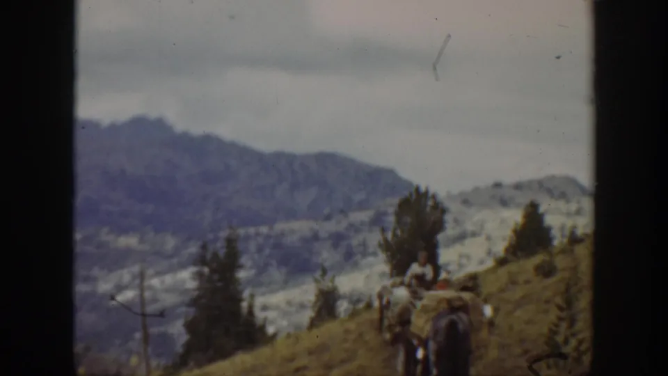A distant rider and pack animal continue across a California mountain hillside in faded 1938 8mm footage.