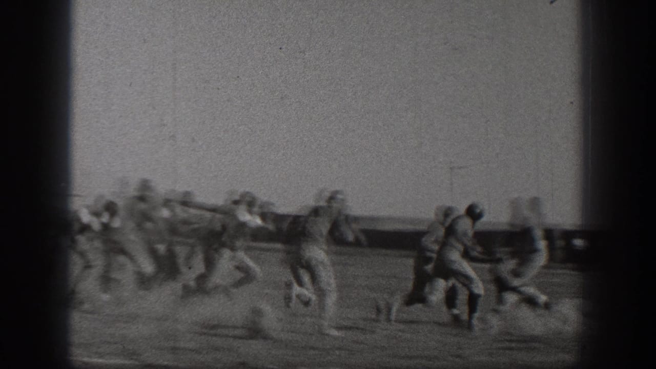 Uniformed football players in 1938 Washington footage appear in motion during a running play, with a field barrier and goal posts visible behind them.