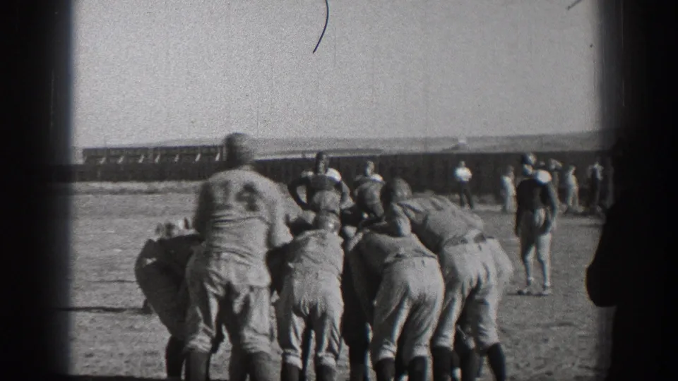 1938 Washington home-movie frame showing helmeted football players clustered at the line on an outdoor grass field.
