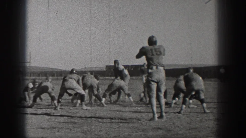 A Washington 1938 home-movie frame shows football players set near the line, with number 15 upright behind them.