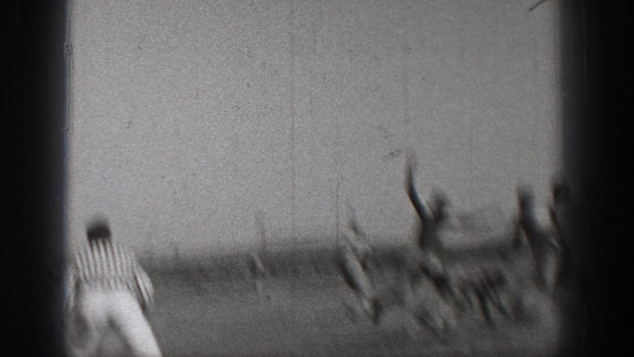 1938 Washington home-movie frame showing blurred football players in motion on an open field as a striped referee watches from the side.