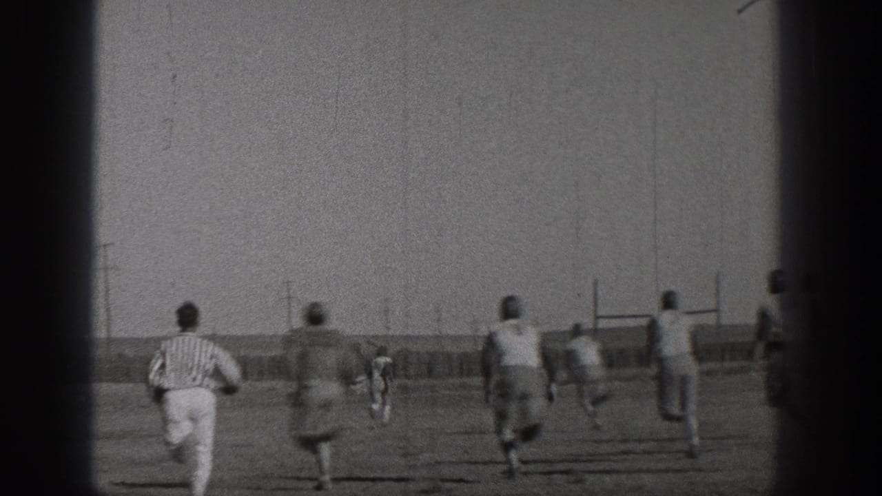 Football players and a referee run toward goal posts on an open field.