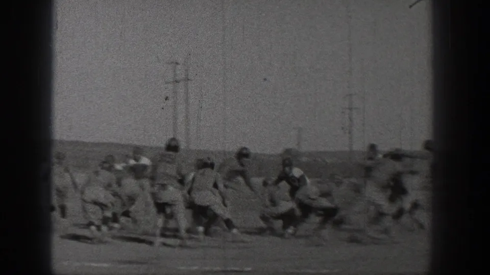 Black-and-white 8mm frame of a 1938 football play in Washington, with players bunching together on the field near utility poles.