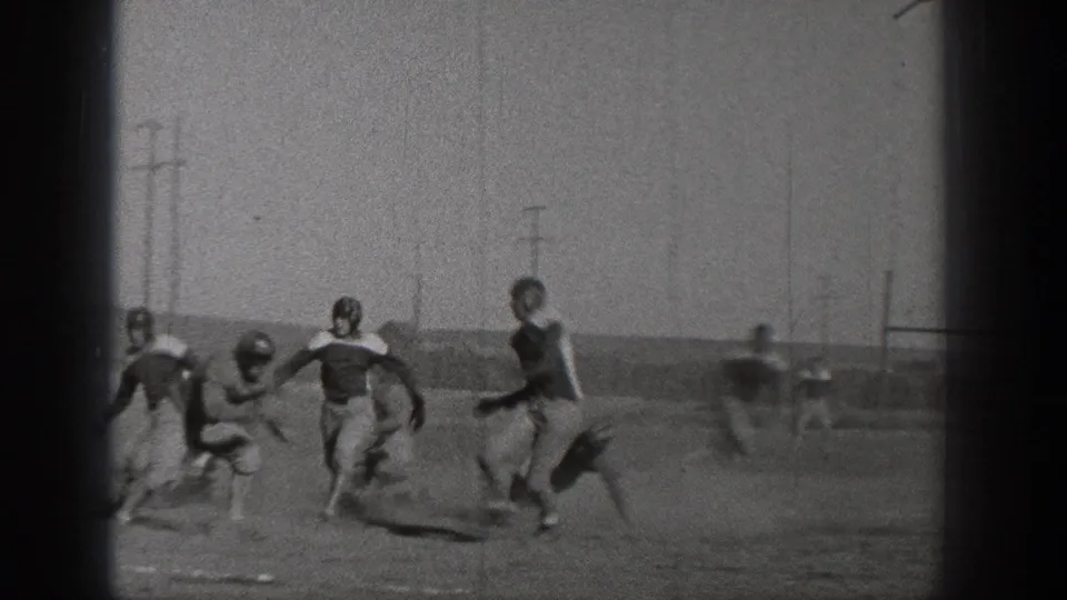 1938 Washington football frame showing players in helmets moving across the field, with utility poles and goal posts in the background.