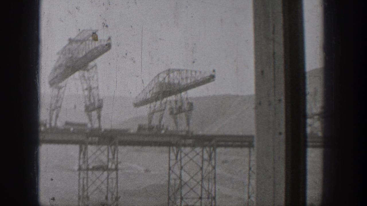 Steel truss structures and lattice supports seen through dark vertical window frames.