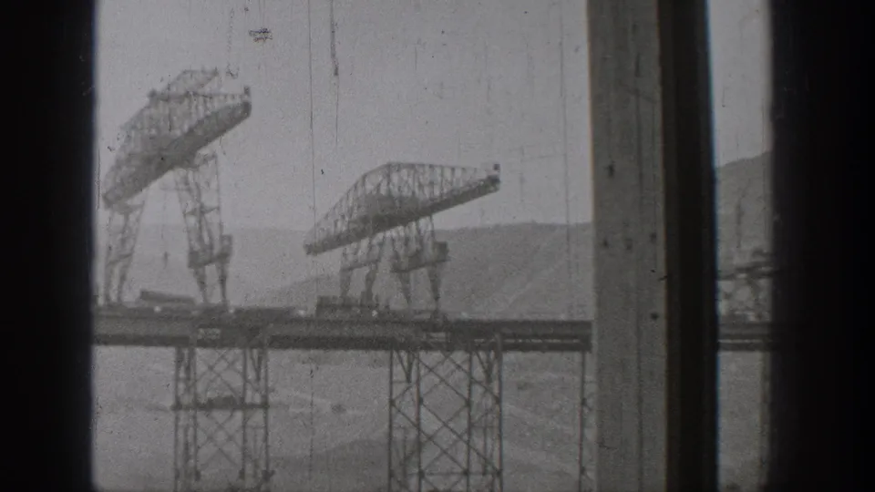 1938 Washington home-movie view of elevated trusswork and support towers across water, framed by dark interior window divisions.
