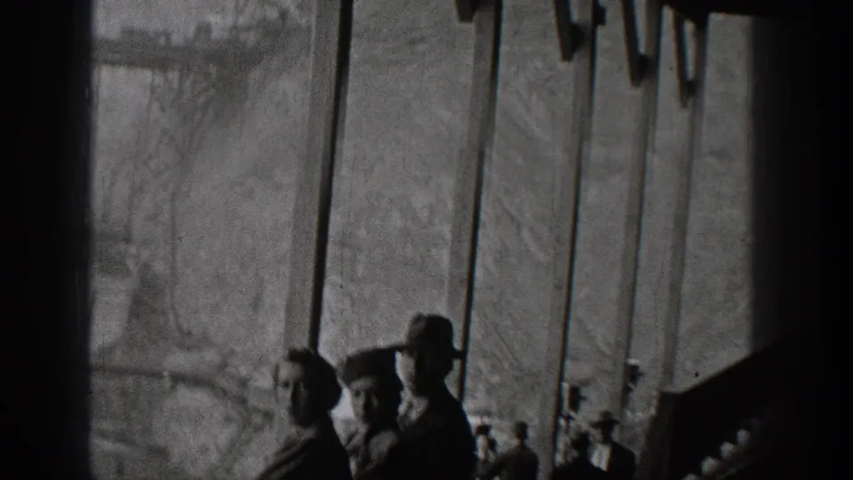 Interior 8mm frame with dark silhouetted figures or shapes near a window, looking toward industrial structures outside in Washington.