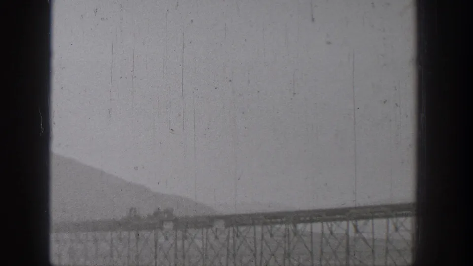 1938 Washington 8mm view of a long elevated industrial span or trestle across water, with hazy hills and scratched film texture.