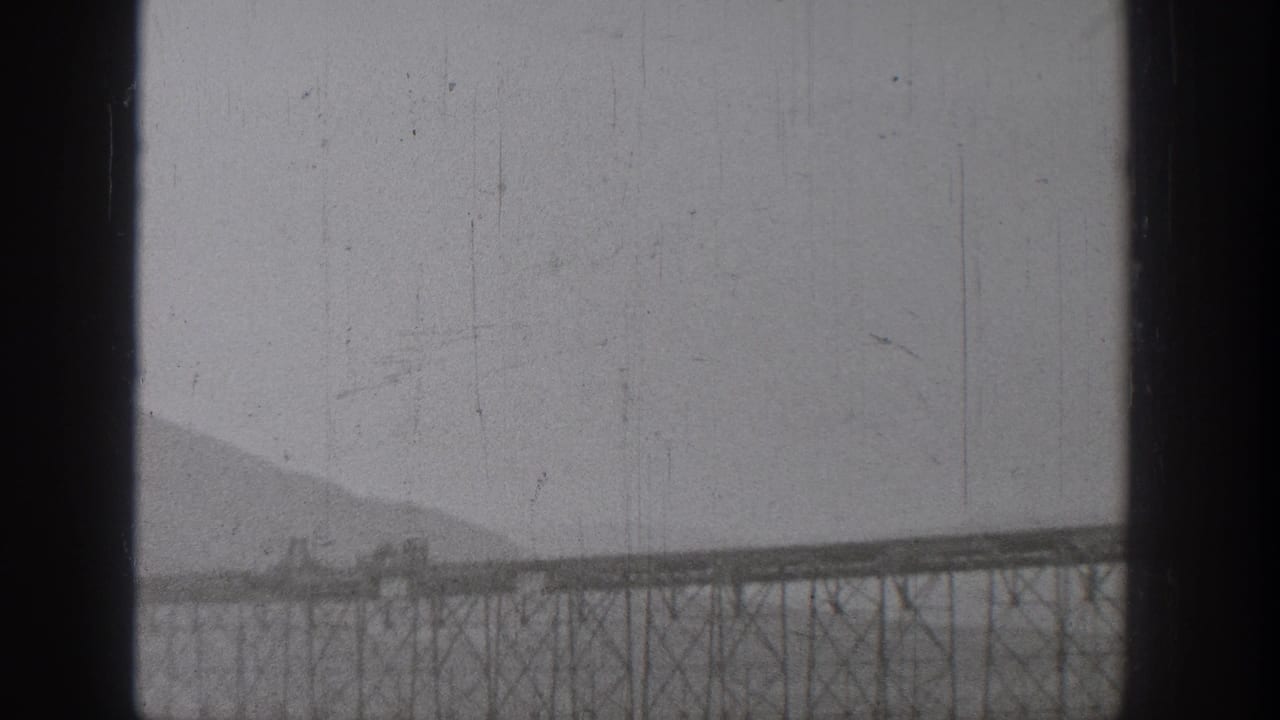 1938 Washington home-movie frame showing a distant steel trestle bridge across a river landscape with mountains behind it.
