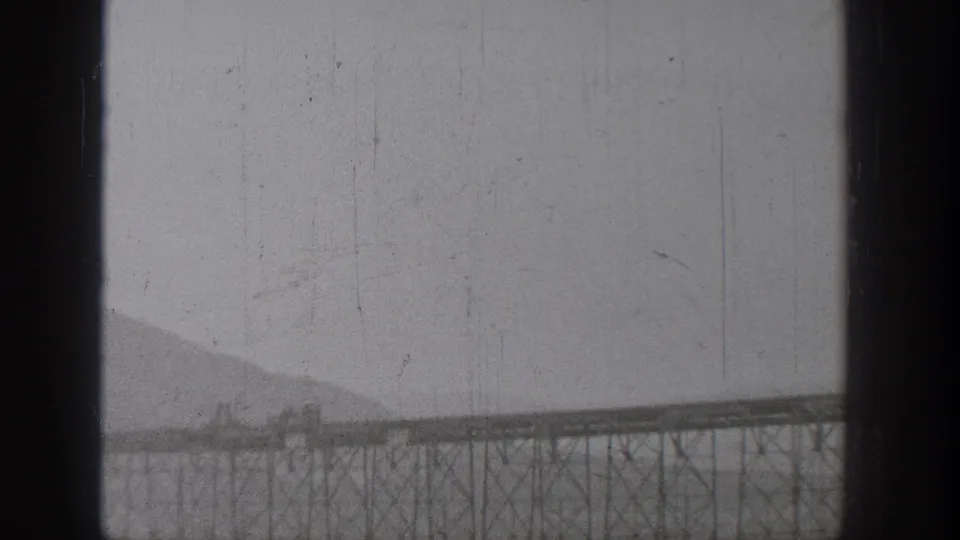 1938 Washington home-movie frame showing a distant steel trestle bridge across a river landscape with mountains behind it.