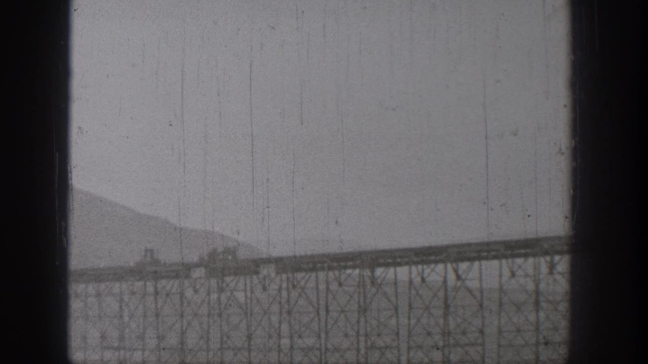Distant train crossing a long steel bridge against a mountain backdrop.