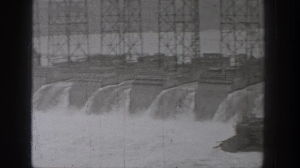 1938 Washington frame showing water pouring over a dam spillway beneath or near a long steel bridge.
