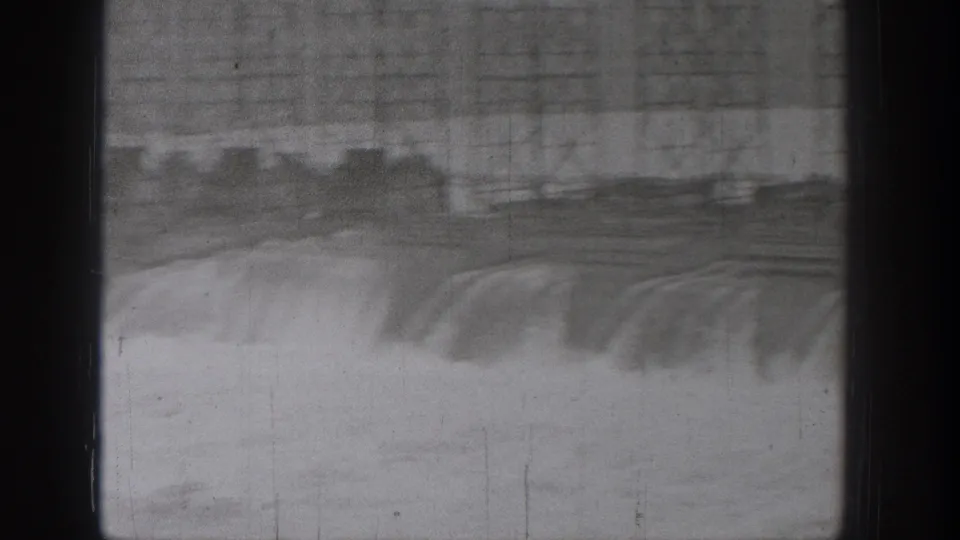 1938 Washington home-movie frame showing turbulent river water beneath a large bridge or spillway, seen through dark vertical divisions.