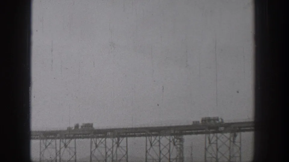 1938 Washington home-movie frame of a long steel bridge carrying vehicles across a broad river, with visible truss supports below.