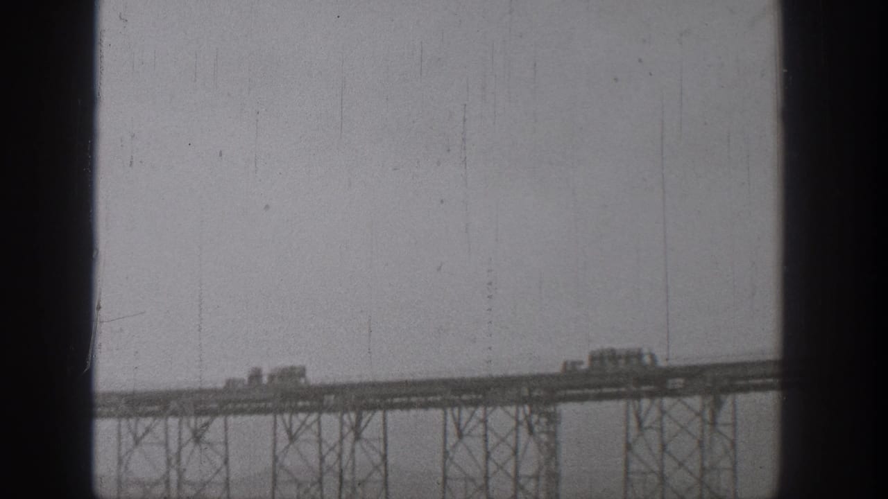 1938 Washington home-movie frame showing trucks or cars moving across a distant elevated steel bridge.