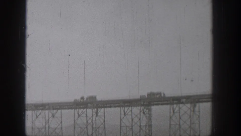 1938 Washington 8mm frame with trucks and cars crossing a long truss-like bridge structure.