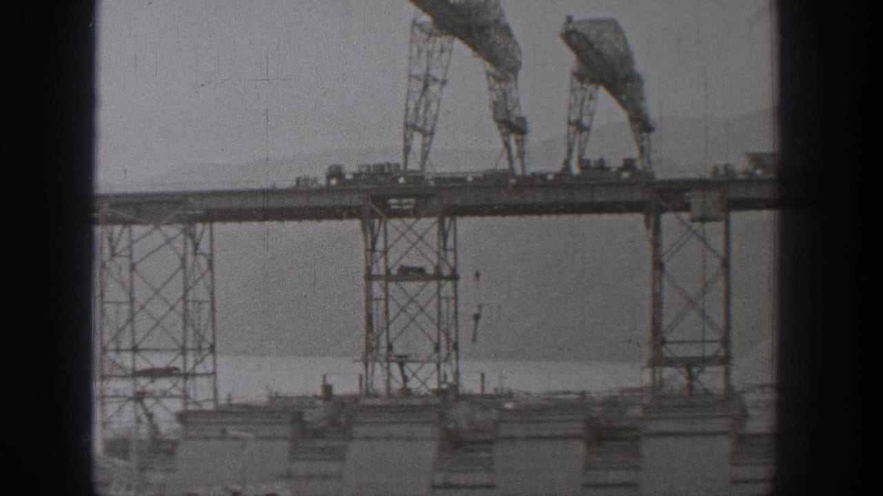 1938 Washington 8mm frame showing tall gantry-like machinery and suspended hooks over a waterfront industrial area.