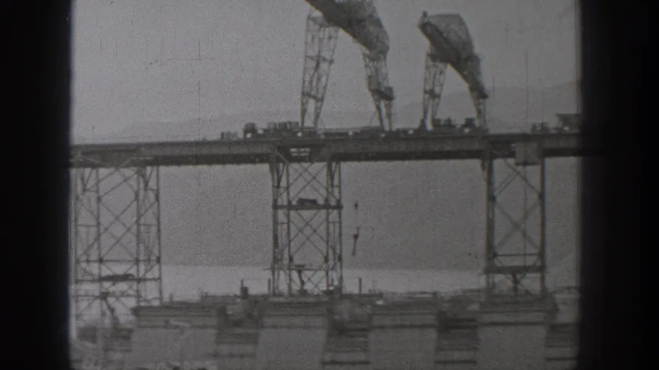 1938 Washington 8mm frame showing tall gantry-like machinery and suspended hooks over a waterfront industrial area.