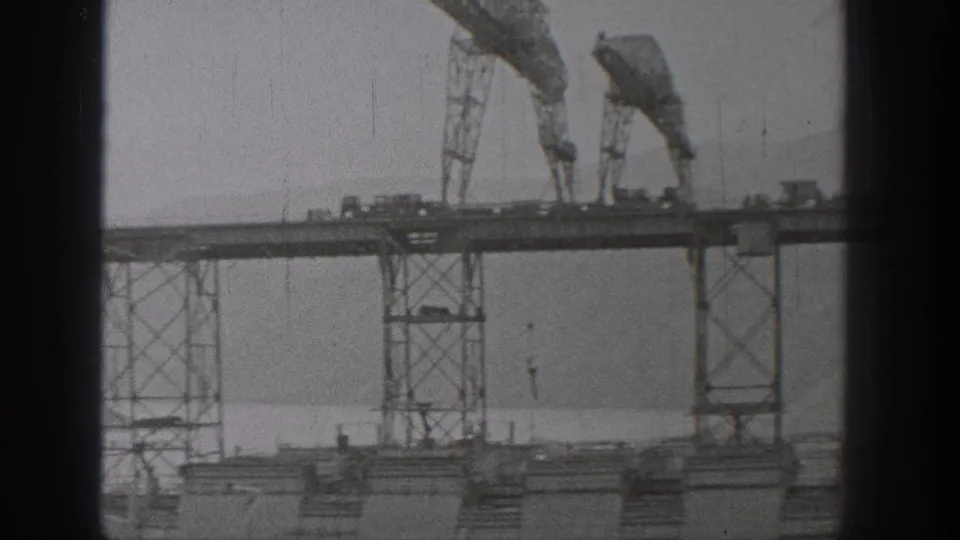 1938 Washington 8mm frame showing a bridge span under construction with cranes, steel supports, and haze beyond.