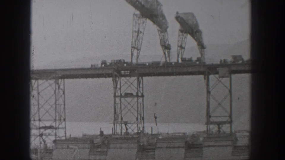 1938 Washington frame with cranes over a partially completed steel bridge and vehicles on the elevated span.