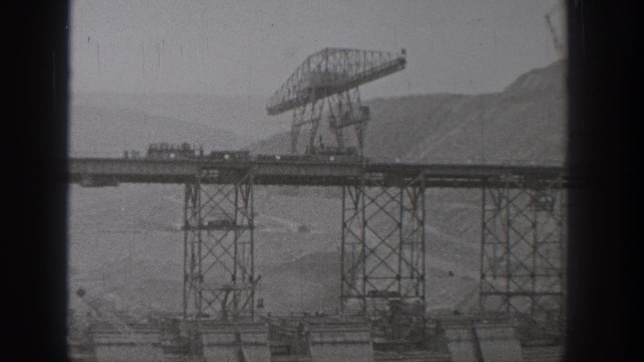 1938 Washington 8mm frame showing an incomplete steel bridge span with a large gantry crane and hazy hills in the background.