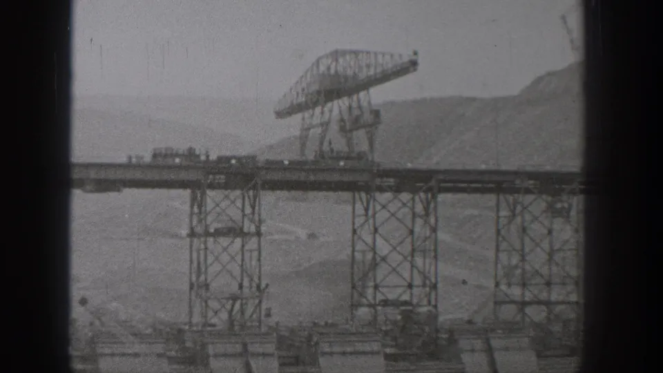 1938 Washington 8mm frame showing an incomplete steel bridge span with a large gantry crane and hazy hills in the background.