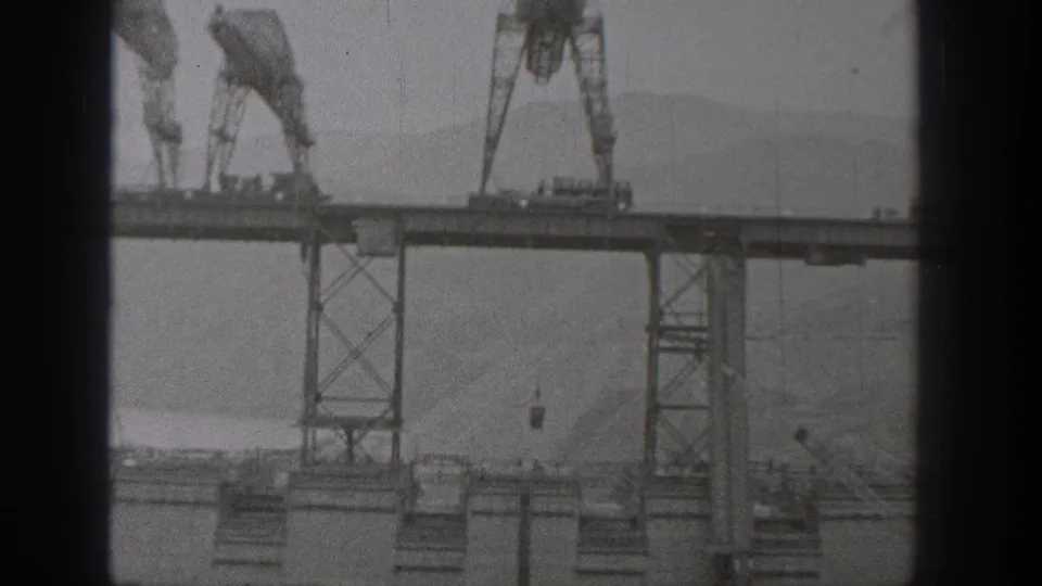 1938 Washington bridge-construction view with multiple gantry cranes on the incomplete deck and hazy terrain behind the structure.