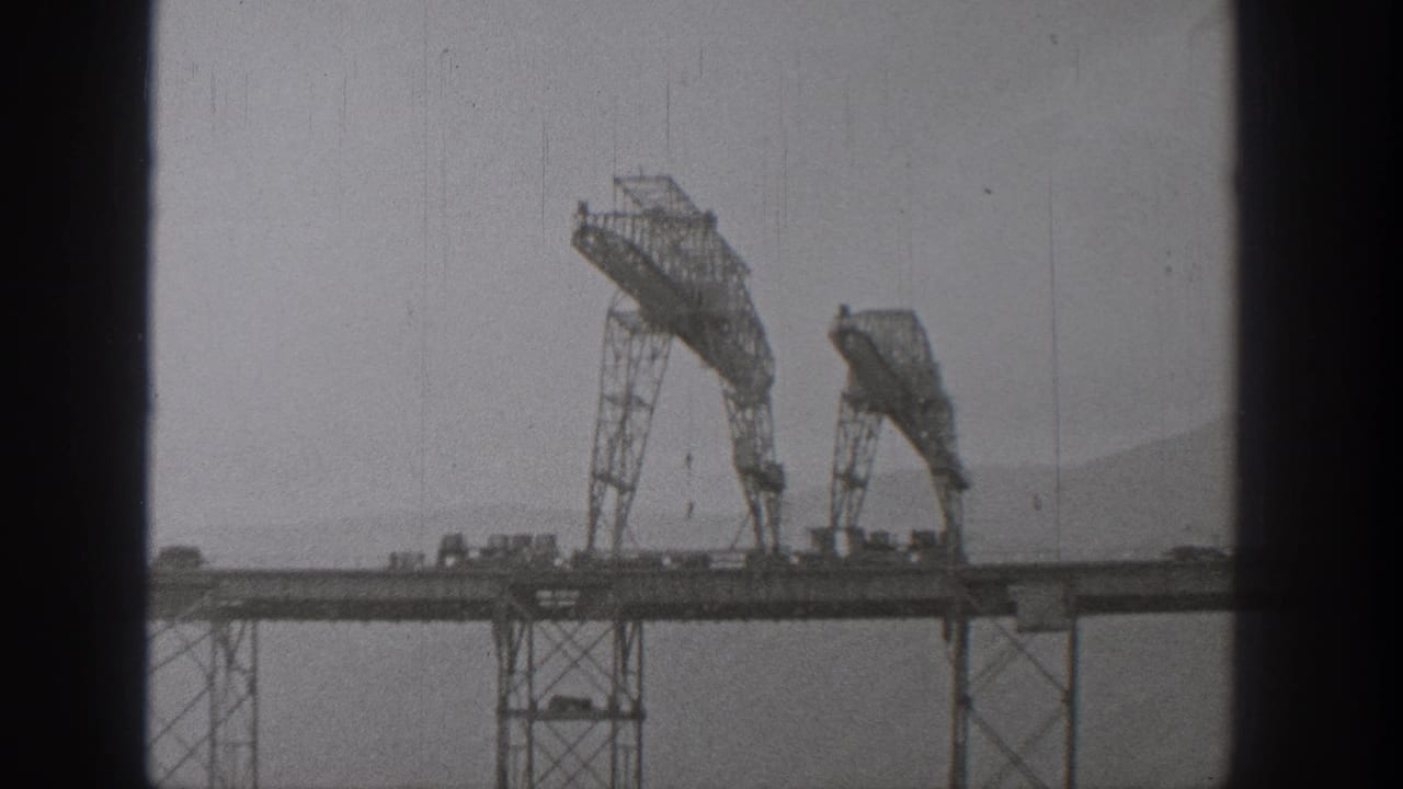 1938 Washington 8mm frame showing large steel bridge-construction equipment over an elevated deck, with water and hills in the distance.