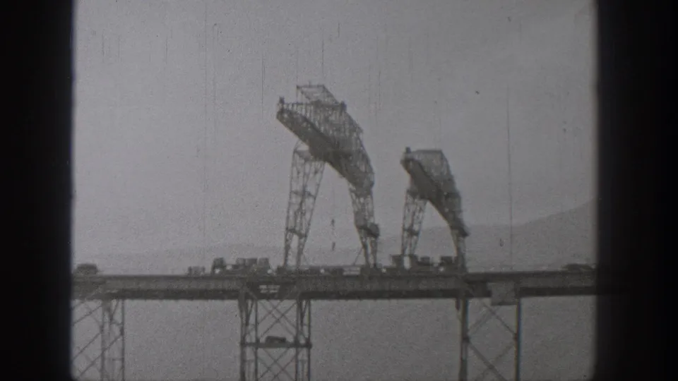 1938 Washington 8mm frame showing large steel bridge-construction equipment over an elevated deck, with water and hills in the distance.