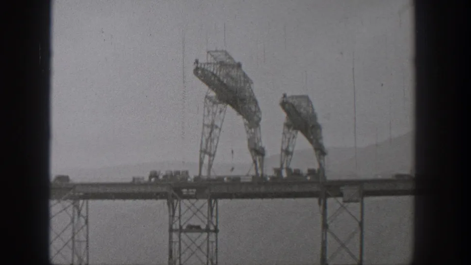 1938 Washington 8mm frame of two arched construction rigs on a bridge deck, partially obscured by dark vertical window or film-frame edges.