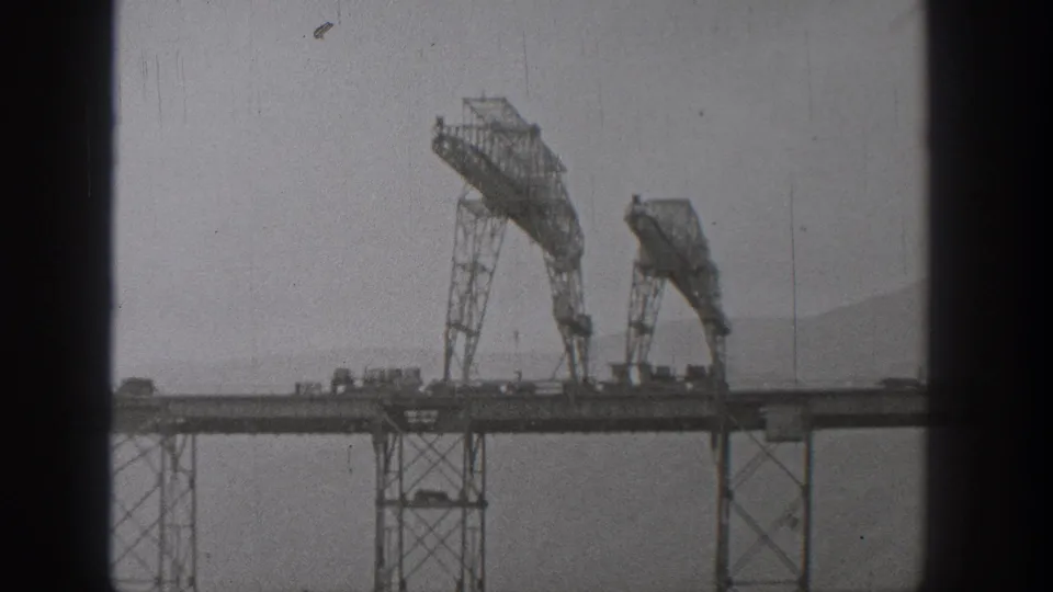 1938 Washington 8mm frame showing bridge-construction rigs and vehicles on an elevated deck, with scratches and dust visible in the scan.