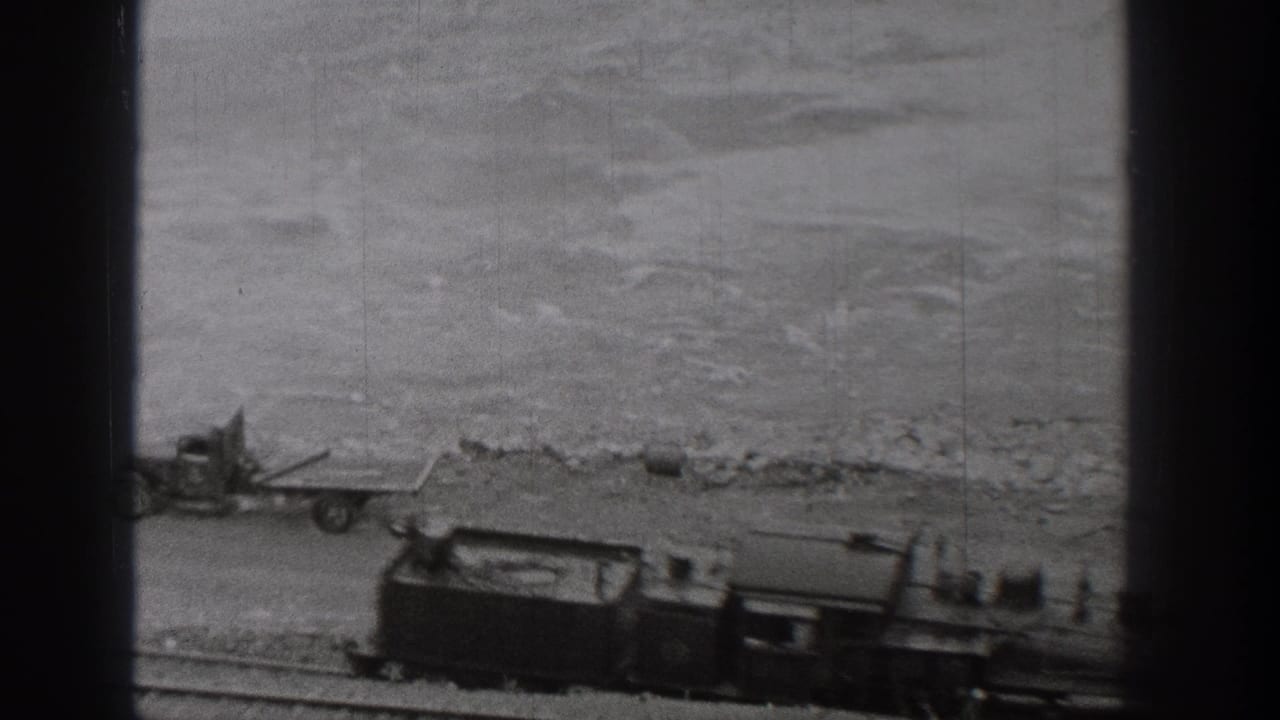 1938 Washington home-movie frame showing a steam train moving along riverside tracks, seen through dark vertical window framing.