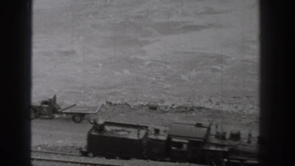 1938 Washington home-movie frame showing a steam train moving along riverside tracks, seen through dark vertical window framing.